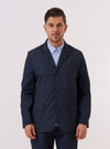 A model wears the Navy Recycled Polytech Capitol Jacket over a light-colored shirt, standing against a plain white background. The jacket is a three-button blazer style with a notch lapel and two large patch pockets at the waist. The model is shown from the front, highlighting the clean, structured fit of the navy blue garment.