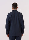 A model wears the Navy Recycled Polytech Capitol Jacket over a light-colored top, shown from the back against a plain white background. The jacket features a clean, structured silhouette with a central seam and a small brand tag at the side. The model is standing with their arms at their sides.
