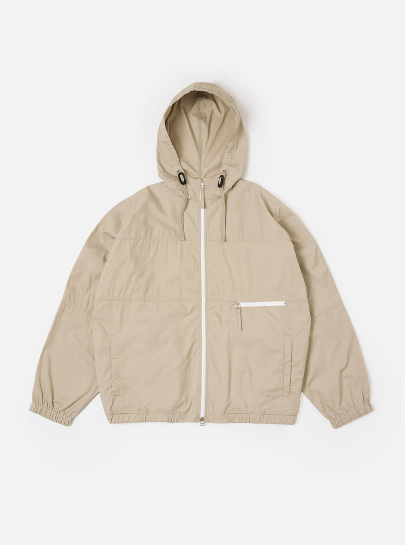 The Sand Cotton Recycled Nylon Mix Daley Jacket is shown as a flat lay against a white background. The jacket features a central zip front, a stand-up collar, and two large zipped patch pockets at the waist. The fabric is a smooth, sand-colored cotton and recycled nylon blend with visible panelling details.