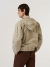 A model wears the Sand Cotton Recycled Nylon Mix Daley Jacket, shown from a rear three-quarter angle against a plain white background. The jacket features a spacious hood, a relaxed fit, and a straight hem. The sand-colored fabric has a smooth, matte finish. No mannequin is present in the image.