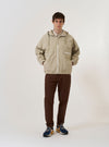 The Sand Cotton Recycled Nylon Mix Daley Jacket is shown as a flat lay against a plain white background. The jacket features a full-zip front, a spacious hood with a high neckline, and two large slanted patch pockets at the waist. The lightweight fabric is a solid sand color with a smooth, technical finish.
