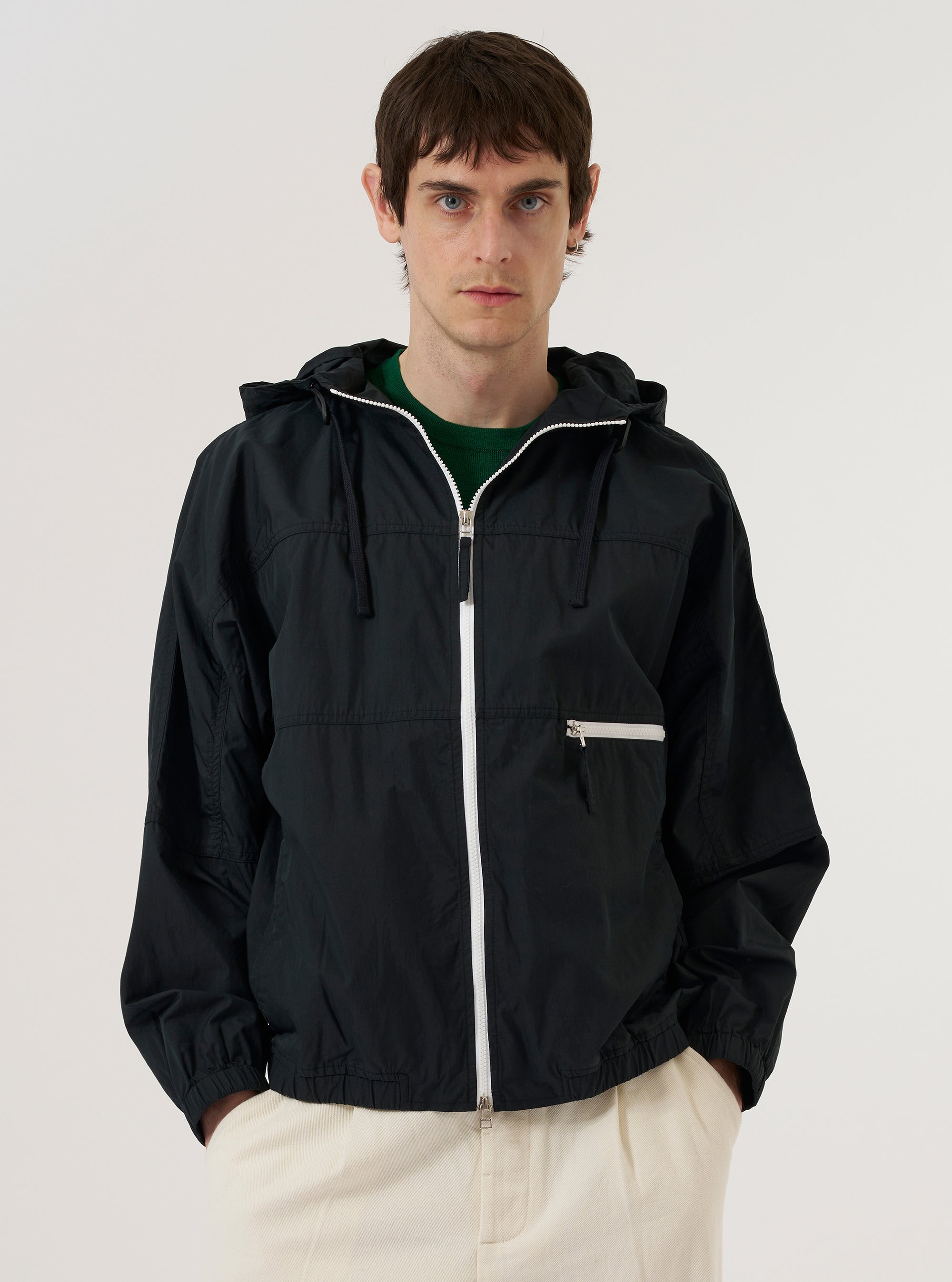 A model wears the Navy Cotton Recycled Nylon Mix Daley Jacket against a plain white background. The jacket is a hooded zip-up style featuring a central zipper, a drawstring hood, and two large patch pockets at the waist. The model is shown from the front, wearing the jacket over a light-colored top. The fabric has a smooth, matte finish.