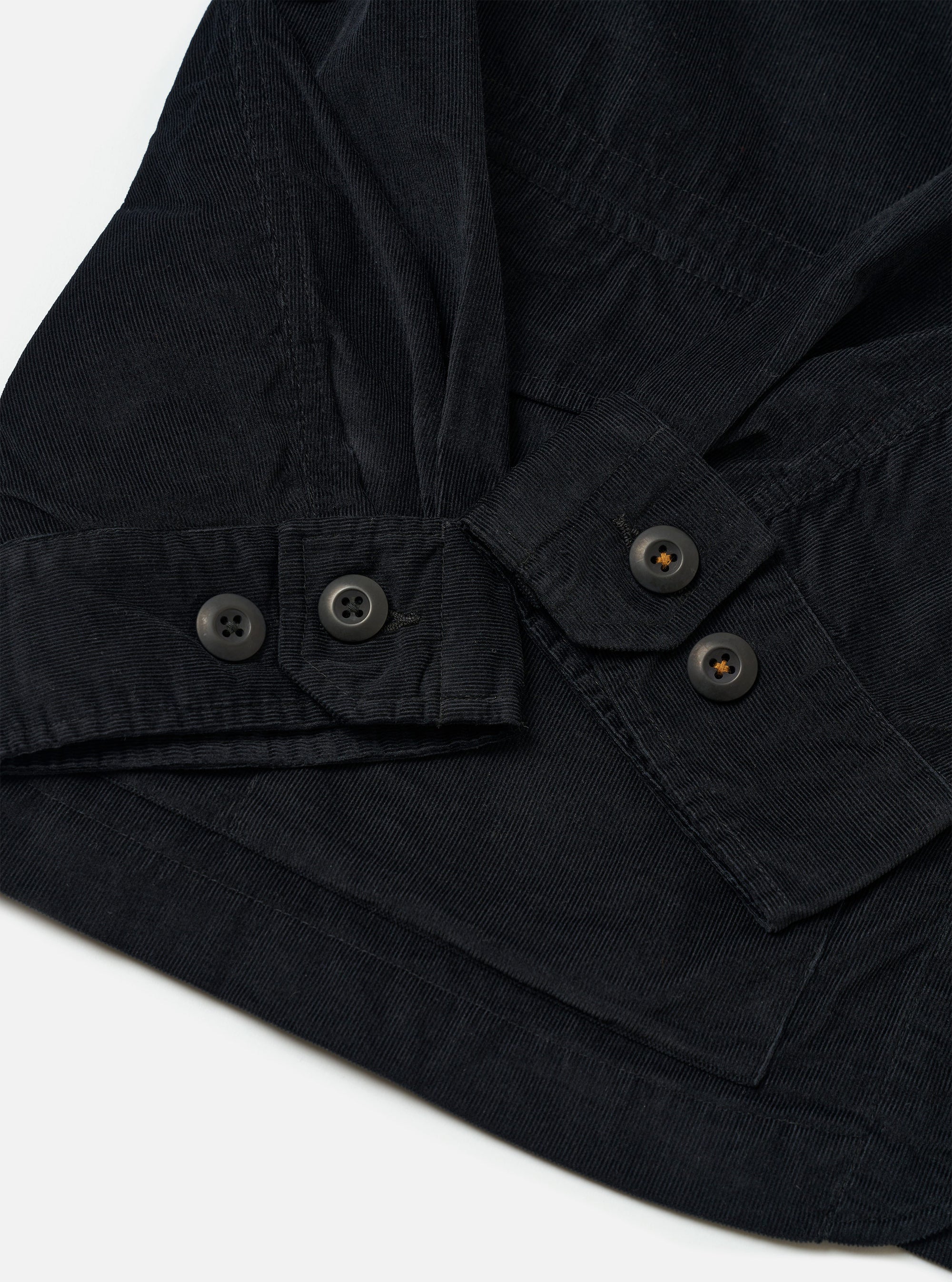 The Black Organic Fine Cord Duty Jacket is shown in a detail view as a flat lay against a white background. This shot focuses on the upper section of the jacket, highlighting the classic spread collar, the top button of the front placket, and the fine texture of the black corduroy fabric.