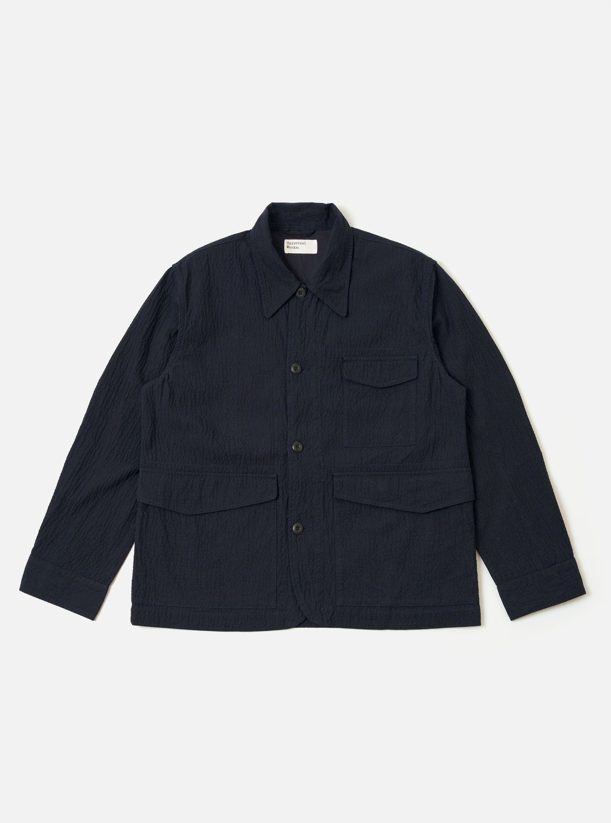 The Dark Navy Ospina Cotton Duty Jacket is presented as a flat lay against a plain white background. The jacket features a five-button front closure, a structured collar, and three prominent patch pockets on the front. The fabric displays a subtle, puckered seersucker texture.