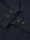 The Dark Navy Ospina Cotton Duty Jacket is shown from the back as a flat lay against a plain white background. The image highlights the clean construction of the shoulders and the straight hem of the jacket. The dark navy fabric features a subtle, puckered seersucker texture throughout.