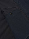 The Dark Navy Ospina Cotton Duty Jacket is shown in a detail view as a flat lay against a plain white background. The image highlights the textured seersucker finish of the dark navy fabric, the clean stitching of the hem, and the curved shape of the lower garment.