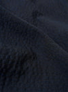 A close-up fabric swatch of the Dark Navy Ospina Cotton Duty Jacket highlights the deep navy blue color and the distinct puckered texture of the seersucker material. The fabric fills the entire frame.