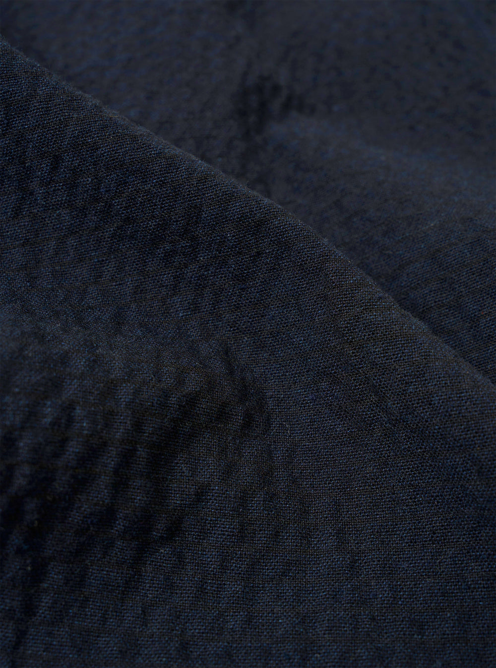 A close-up fabric swatch of the Dark Navy Ospina Cotton Duty Jacket highlights the deep navy blue color and the distinct puckered texture of the seersucker material. The fabric fills the entire frame.