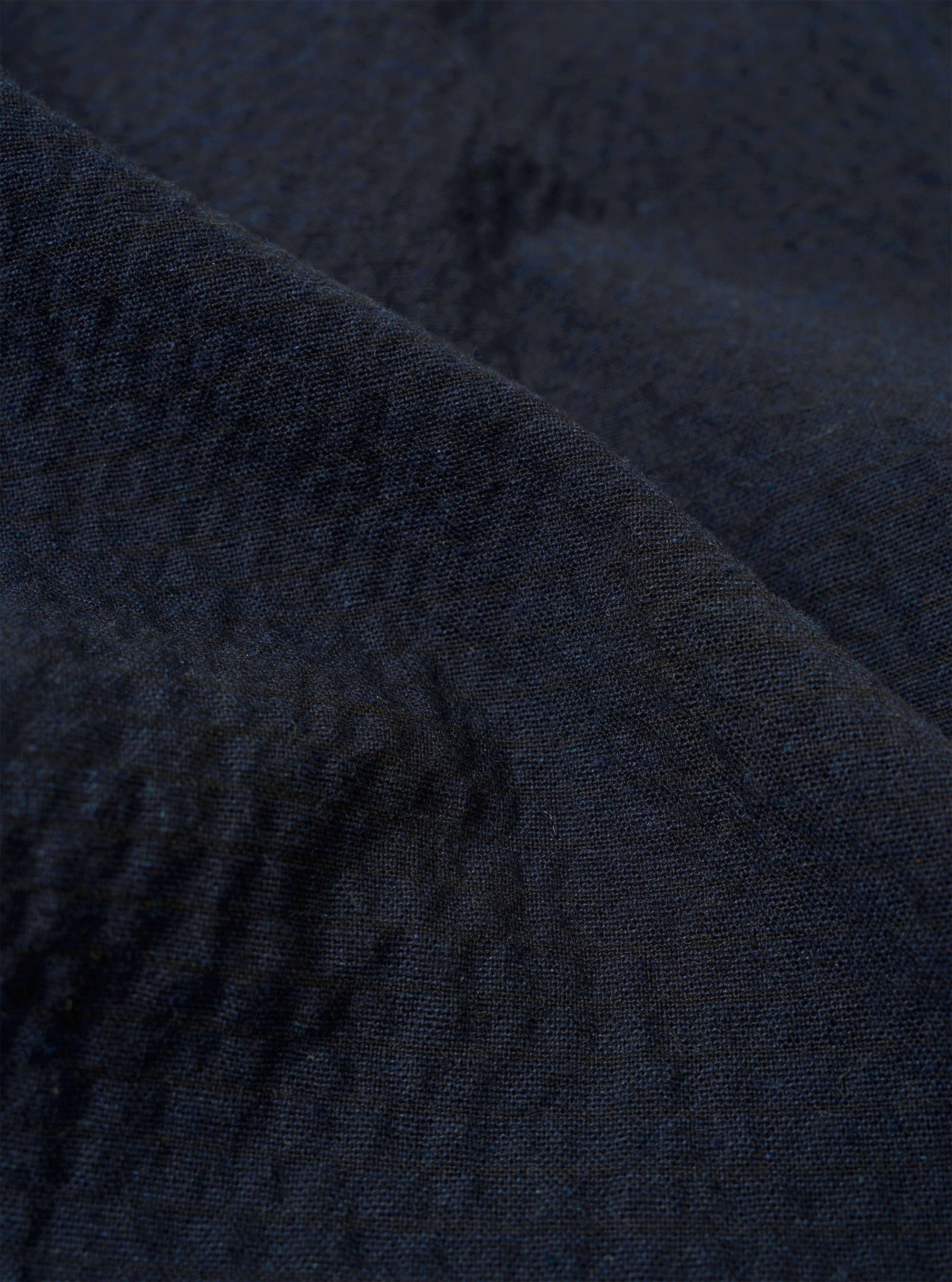 A close-up fabric swatch of the Dark Navy Ospina Cotton Duty Jacket highlights the deep navy blue color and the distinct puckered texture of the seersucker material. The fabric fills the entire frame.