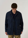 A model wears the Indigo Kaihara LT WT Denim Jungle Jacket over a light-colored top, standing against a plain white background. The jacket is crafted from deep indigo denim and features four large front patch pockets with button closures and a full-length buttoned front.