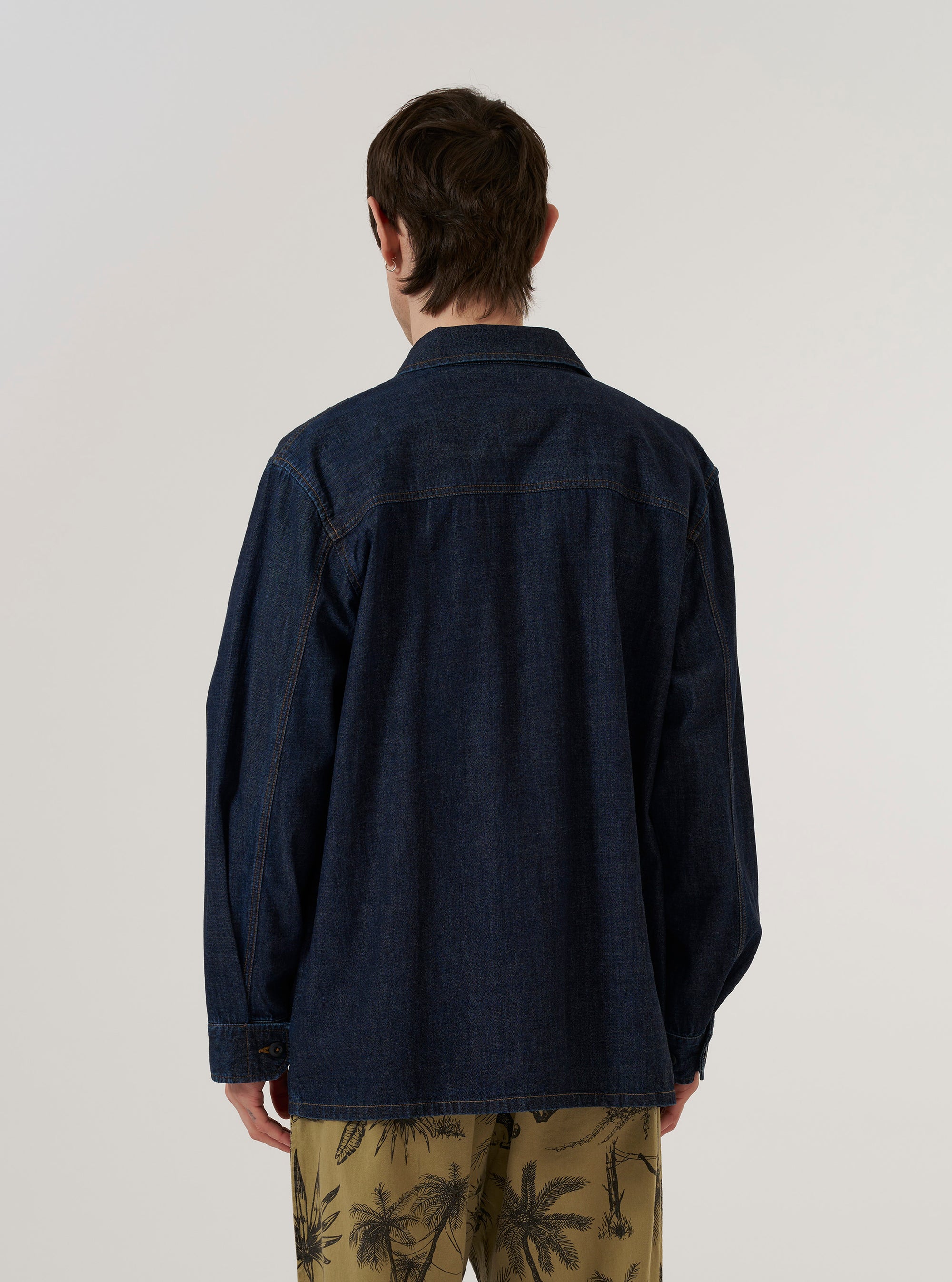 A model wears the Indigo Kaihara LT WT Denim Jungle Jacket over a light-colored shirt, standing against a plain white background. The jacket features four large front patch pockets with buttoned flaps, a classic collar, and is made from indigo-dyed lightweight denim. The image shows the garment from a front angle, highlighting its utility-style construction and the texture of the denim fabric.
