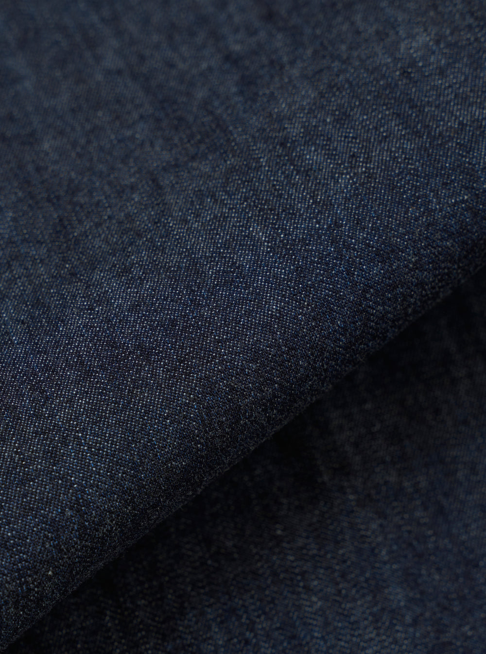 A close-up fabric swatch of the Indigo Kaihara LT WT Denim Labour Jacket highlights the deep indigo blue color and the fine, lightweight weave of the Japanese denim. The textile fills the frame, showcasing a uniform color and smooth surface.