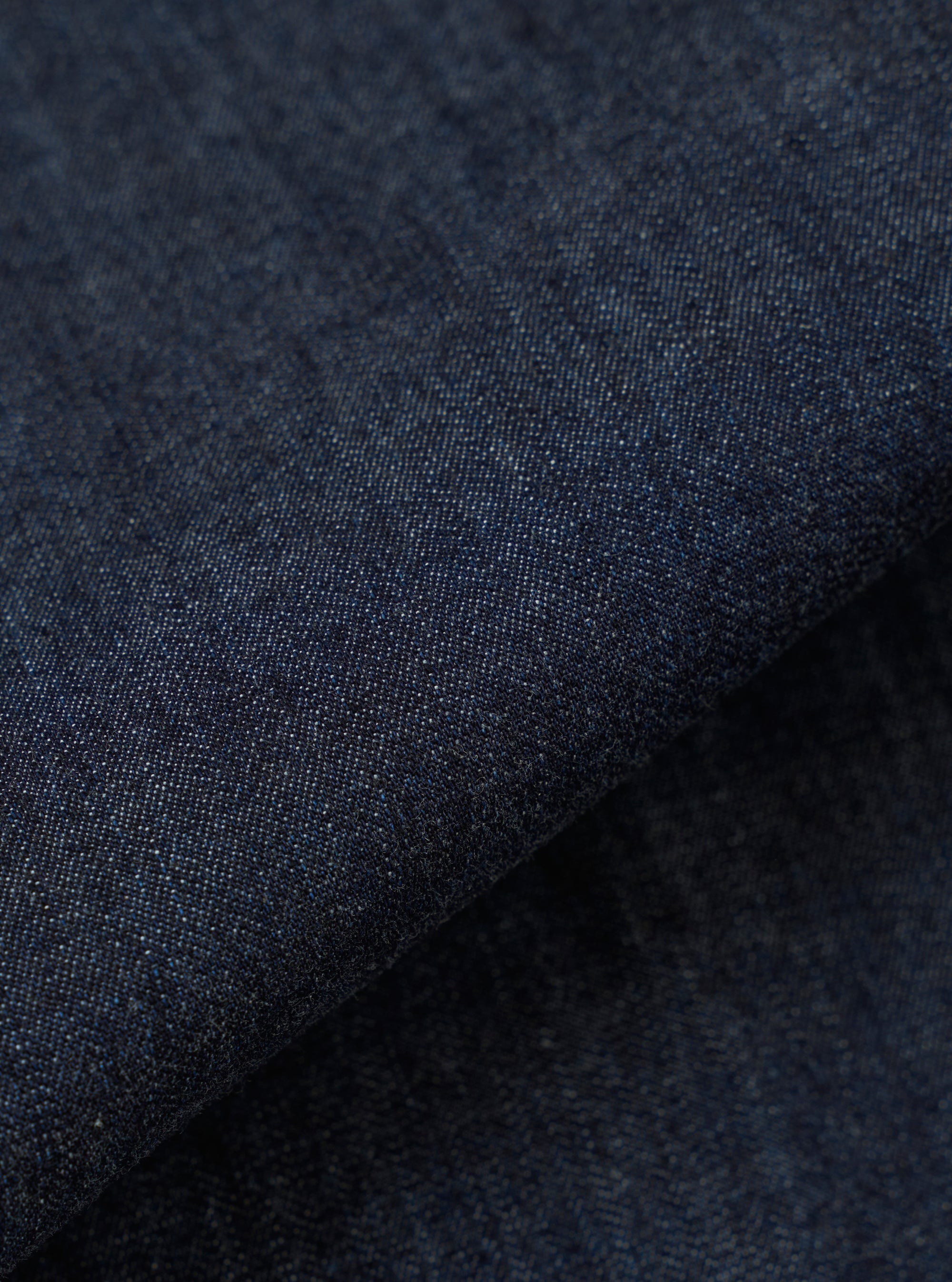 A close-up fabric swatch of the Indigo Kaihara LT WT Denim Labour Jacket highlights the deep indigo blue color and the fine, lightweight weave of the Japanese denim. The textile fills the frame, showcasing a uniform color and smooth surface.