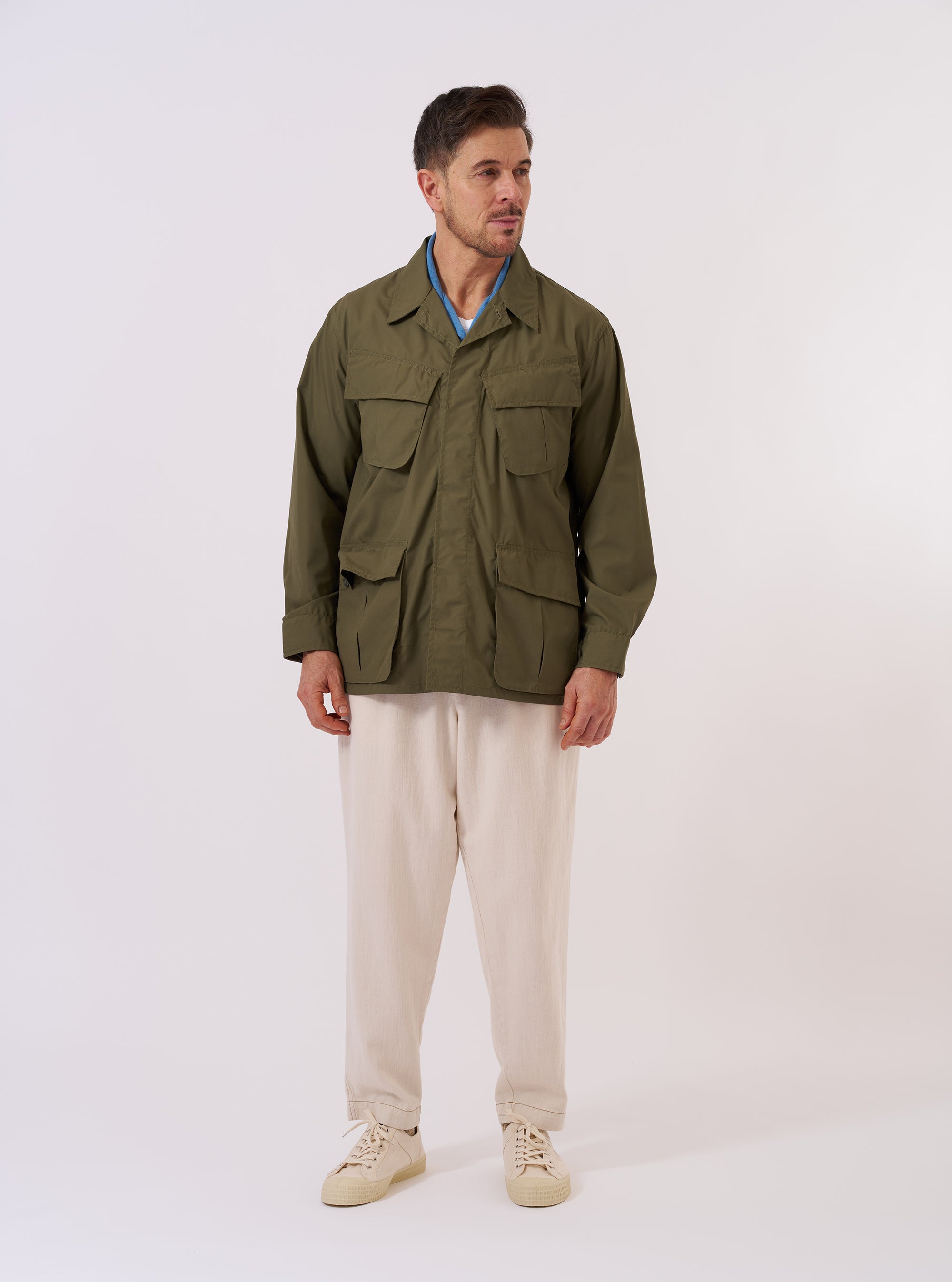 The Olive Recycled Polytech Jungle Jacket is shown as a flat lay against a white background. The jacket features a concealed button front placket and four large 3D pleated pockets with concealed button-down flaps. It has a structured collar and adjustable cuffs.