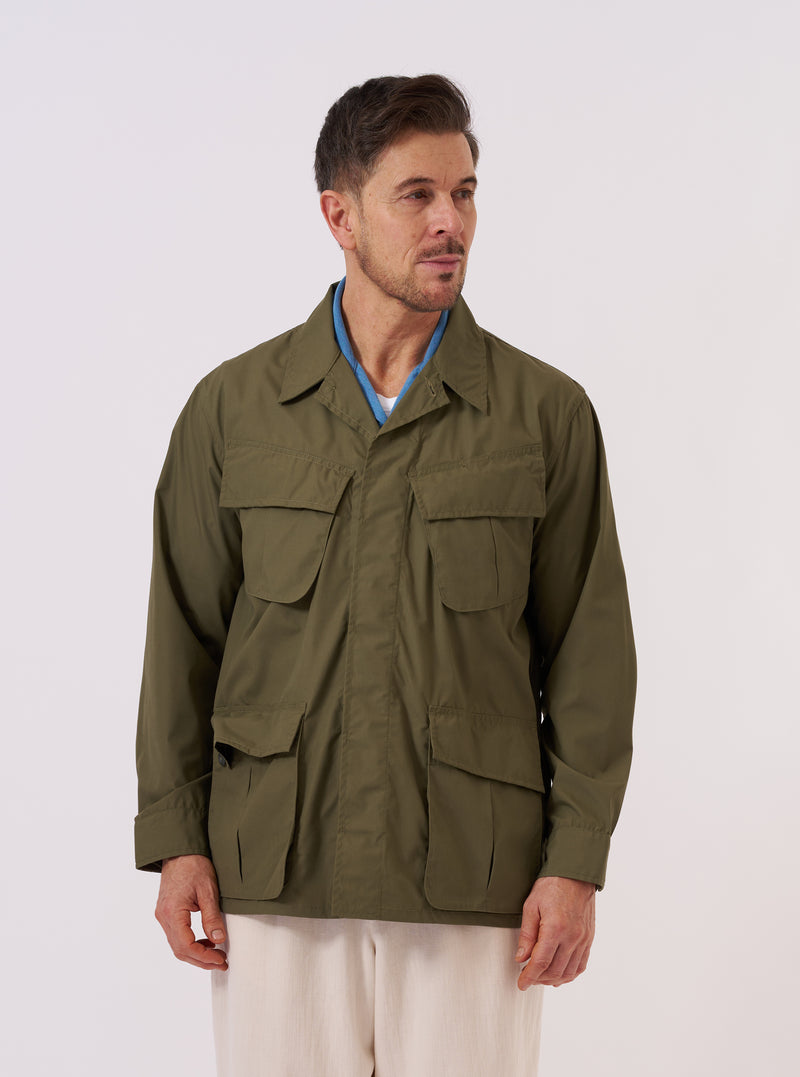 A model wears the Olive Recycled Polytech Jungle Jacket over a light-colored shirt against a plain white background. The jacket features a loose, unstructured fit with four large 3D pleated pockets on the front, a concealed button placket, and wide sleeves with adjustable cuffs. The model is shown from the front, highlighting the utility-style design and the olive green color of the recycled polytech fabric.