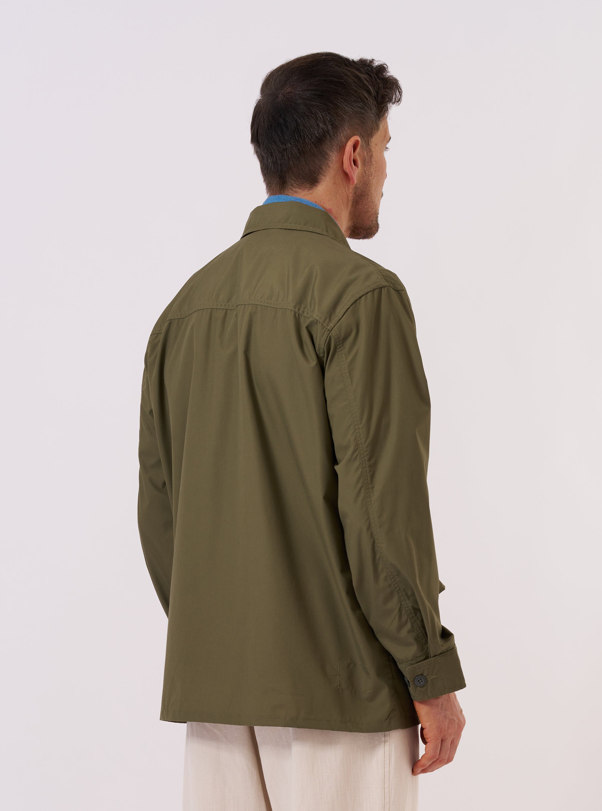 A model wears the Olive Recycled Polytech Jungle Jacket, shown from the back against a plain white background. The jacket's olive green color and utility-inspired design are prominent, highlighting the clean lines of the back panel and the structured shoulder construction. The model is standing in a studio setting.