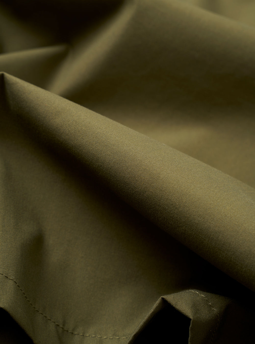 A close-up fabric swatch of the Olive Recycled Polytech Jungle Jacket highlights the olive green color and the fine, technical weave of the material.
