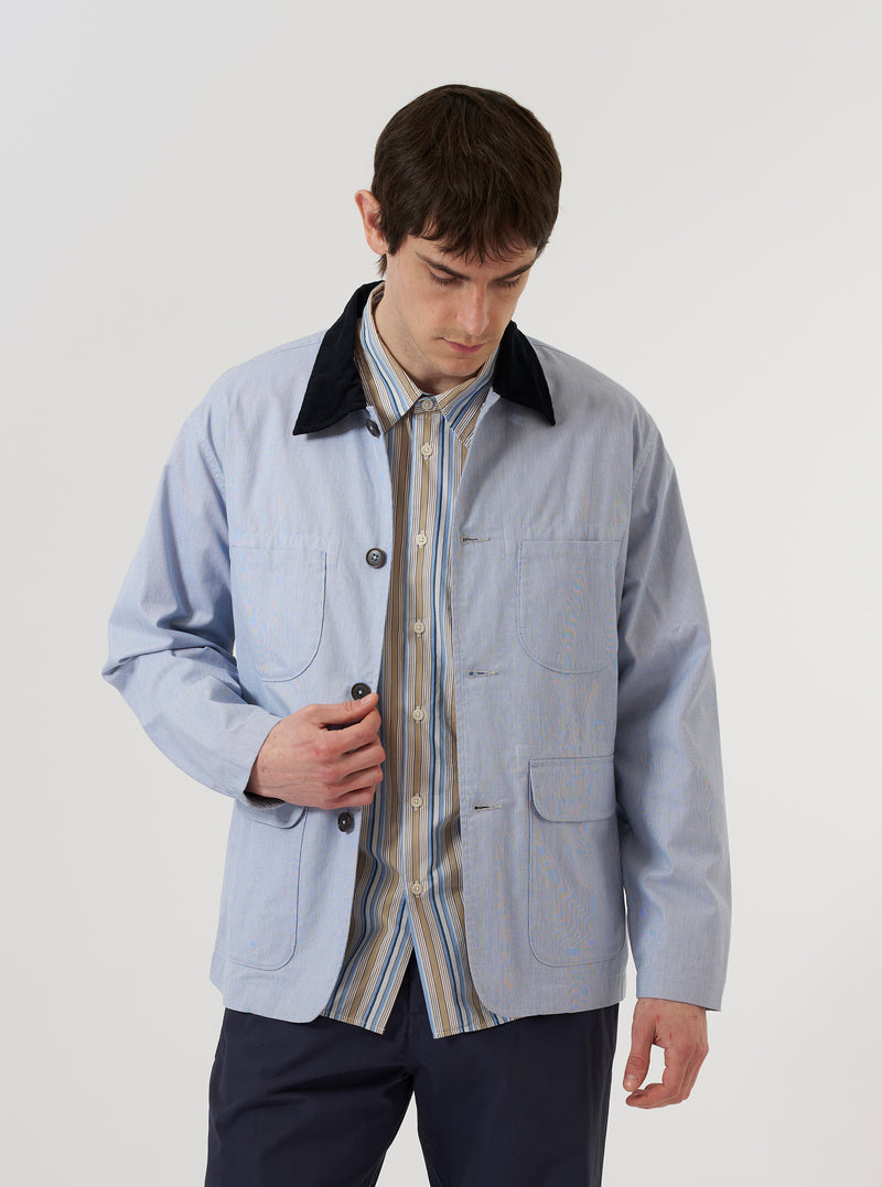A model wears the Navy Kennedy Stripe Labour Jacket while standing against a plain white background. The jacket features a vertical navy and white stripe pattern, a classic collar, a single chest patch pocket, and two large lower patch pockets. The model is shown from the waist up, highlighting the garment's fit and texture.