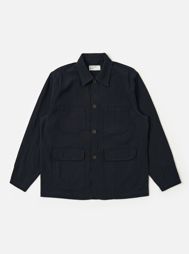 The Dark Navy Ospina Cotton Labour Jacket is shown as a flat lay against a white background. The jacket features a four-pocket design, including two chest patch pockets and two lower patch pockets with flaps. It has a central button-down front and a classic collar. The fabric has a visible seersucker texture.