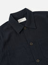 The Dark Navy Ospina Cotton Labour Jacket is shown from the back as a flat lay against a plain white background. The image highlights the jacket's structured back panel, clean seams, and a straight hem. The dark navy fabric features a visible puckered seersucker texture.