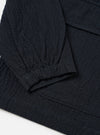 The Dark Navy Ospina Cotton Labour Jacket is shown in a detail view as a flat lay against a plain white background. The image highlights the textured seersucker finish of the navy blue fabric and the construction of the two lower flap patch pockets.