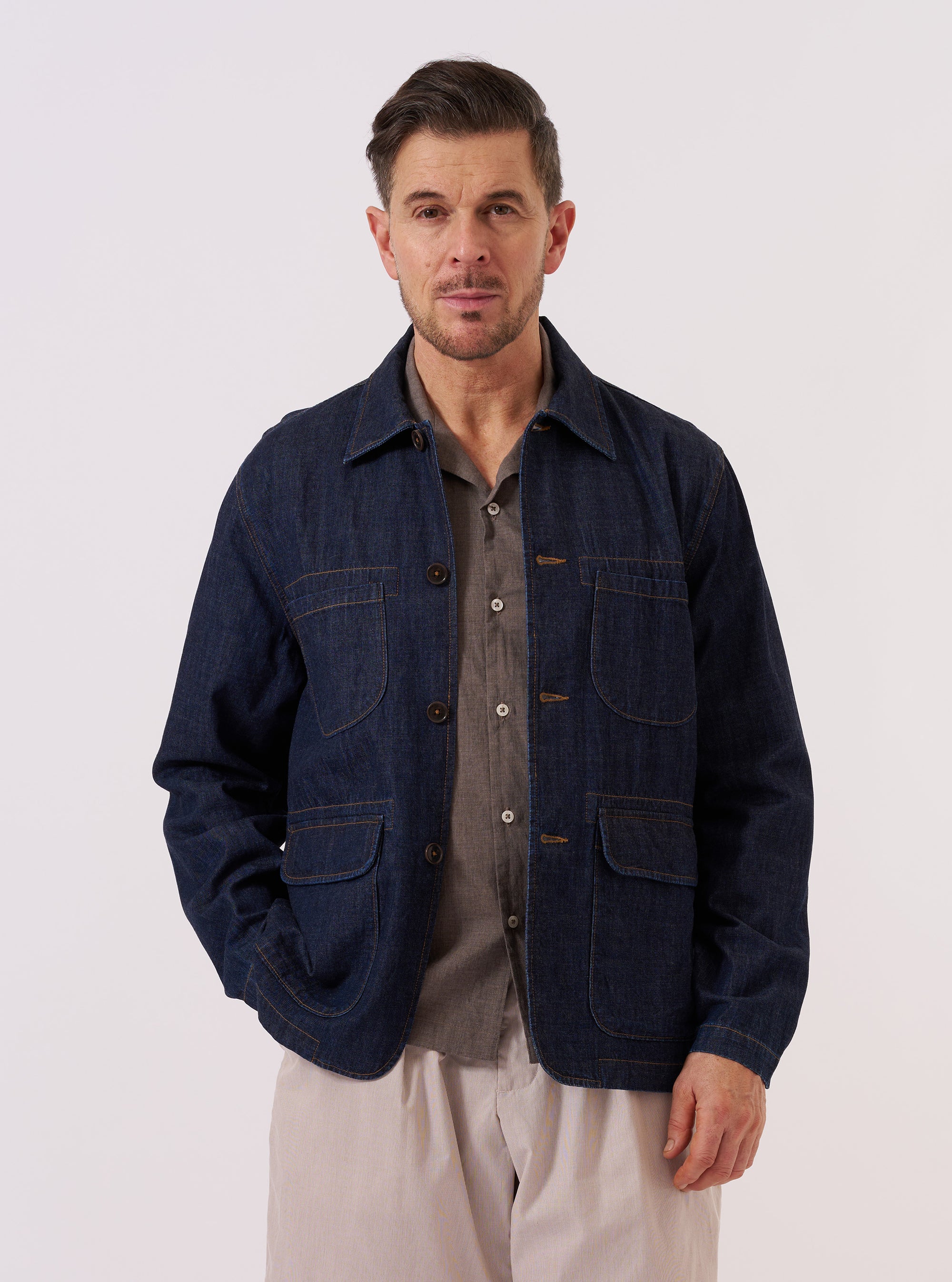 A model wears the Indigo Kaihara LT WT Denim Labour Jacket over a white t-shirt and light-colored trousers against a plain white background. The jacket is a deep indigo blue chore coat featuring a classic collar, a button-down front, and four large front pockets, including two chest pockets and two lower patch pockets. The model is standing and facing forward with their hands at their sides.
