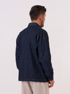 A model wears the Indigo Kaihara LT WT Denim Labour Jacket over a light-colored shirt, shown from a rear three-quarter angle against a plain white background. The jacket features a loose fit, a classic collar, and a visible seam down the center of the back. One lower patch pocket is partially visible on the side.