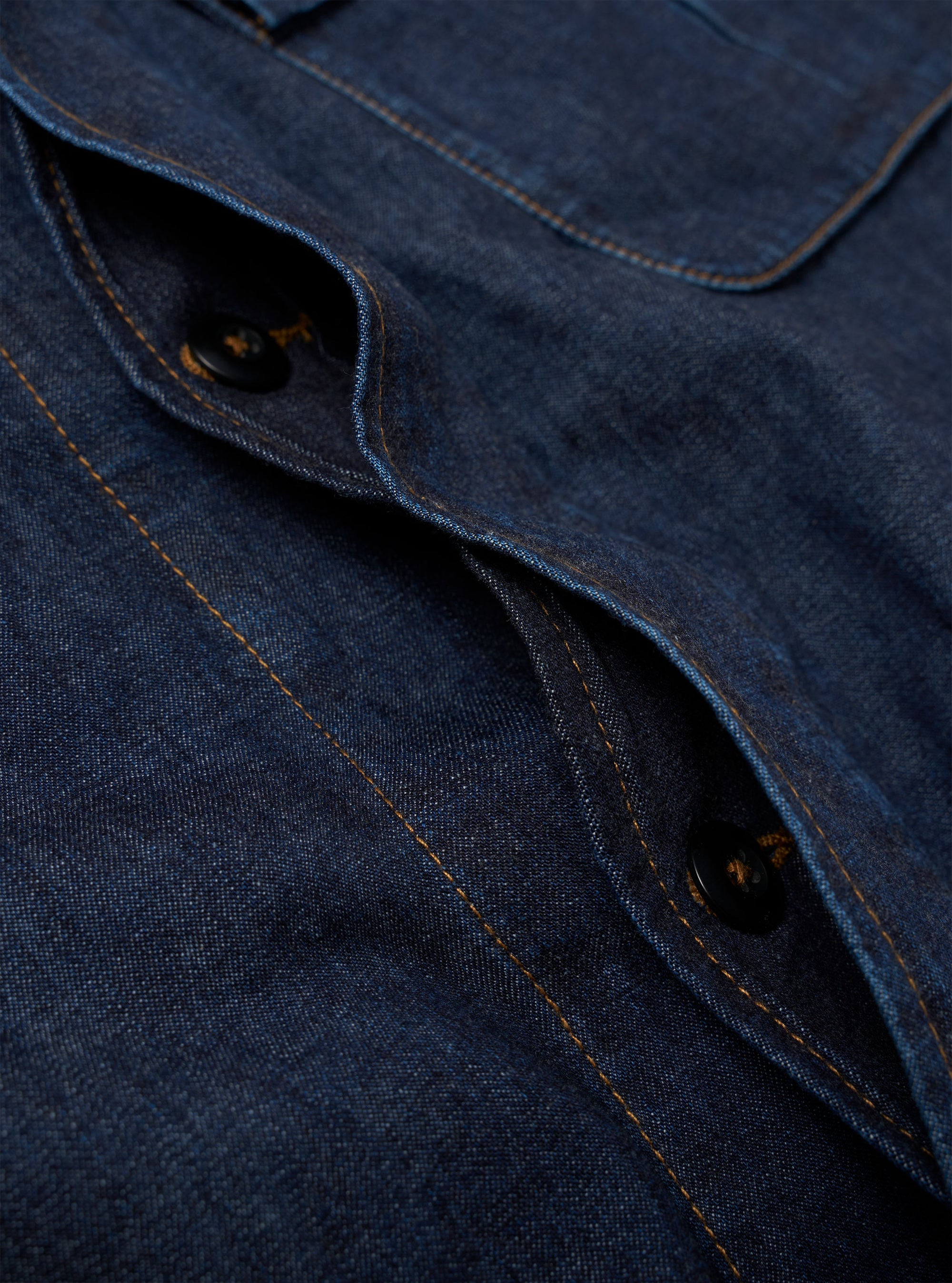 The Indigo Kaihara LT WT Denim Jungle Jacket is shown in a detail view as a flat lay against a plain white background. The image highlights the technical construction of the indigo-dyed cotton denim, focusing on the bottom of the concealed button placket and the two large, pleated, 3D bellowed pockets at the waist.