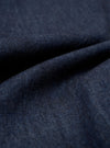 A close-up swatch of the Indigo Kaihara LT WT Denim Jungle Jacket highlights the deep indigo color and the fine diagonal weave of the lightweight Japanese denim fabric. The material fills the frame, providing a detailed view of the textile's texture and natural dye finish.