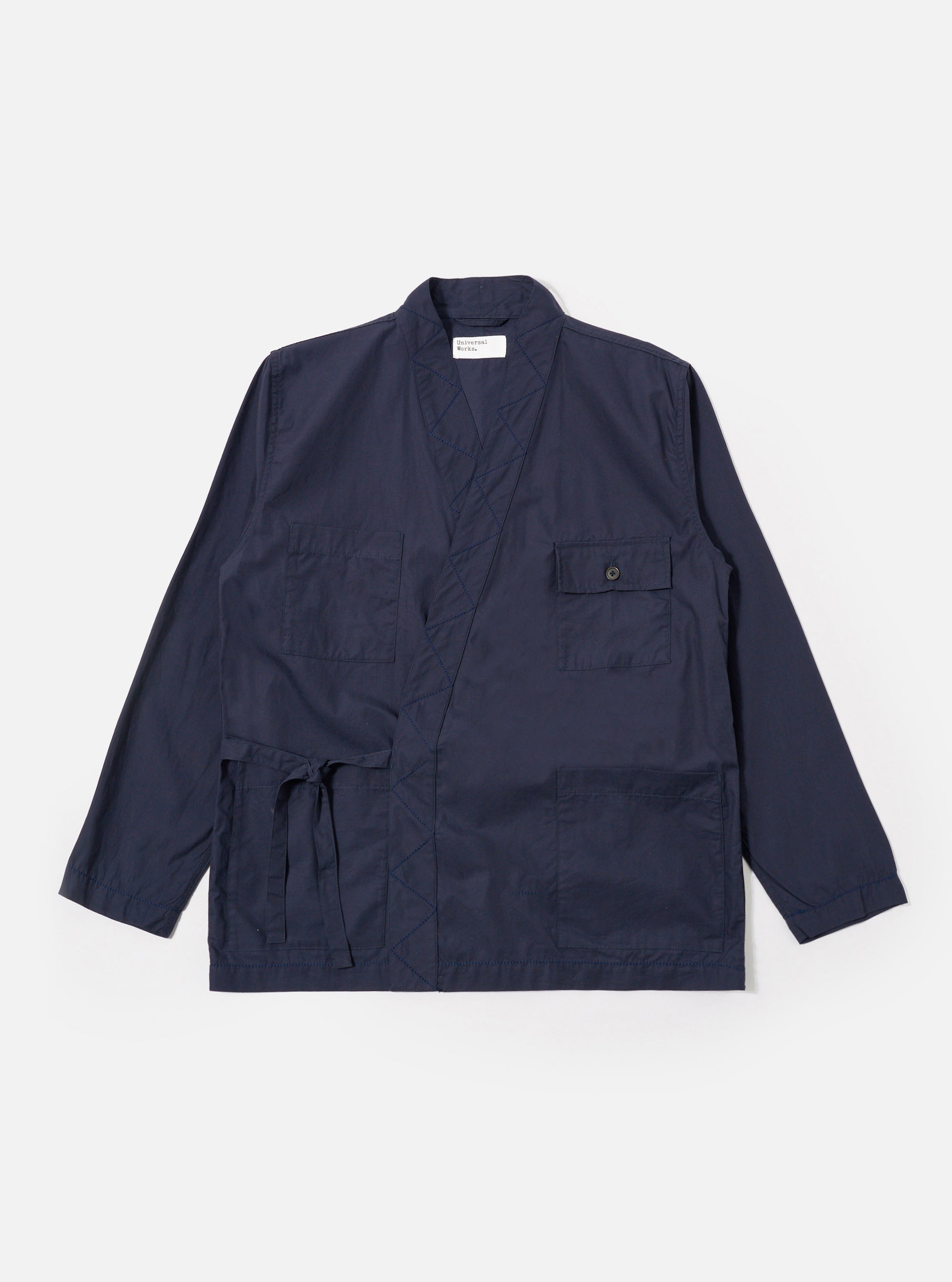 The Navy Peached Poplin Osaka Work Jacket is shown as a flat lay against a plain white background. The jacket features a wrap-front kimono-style design with a V-neckline and tie closures. It includes two large patch pockets at the waist and a single chest pocket. The navy blue cotton fabric has a smooth, matte finish.
