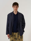 A model wears the Navy Peached Poplin Osaka Work Jacket over a light-colored shirt, standing against a plain white background. The jacket features a wrap-front kimono-style design with an internal tie closure, a simple V-neckline, and two large patch pockets at the waist. The navy blue cotton poplin fabric has a smooth, matte finish.