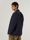 A model wears the Navy Peached Poplin Osaka Work Jacket over a light-colored shirt, shown from a rear three-quarter angle against a plain white background. The jacket features a wrap-style front with internal and external ties, a structured back with a central vertical seam, and a relaxed, kimono-inspired silhouette. The navy cotton fabric has a smooth, matte peached finish.