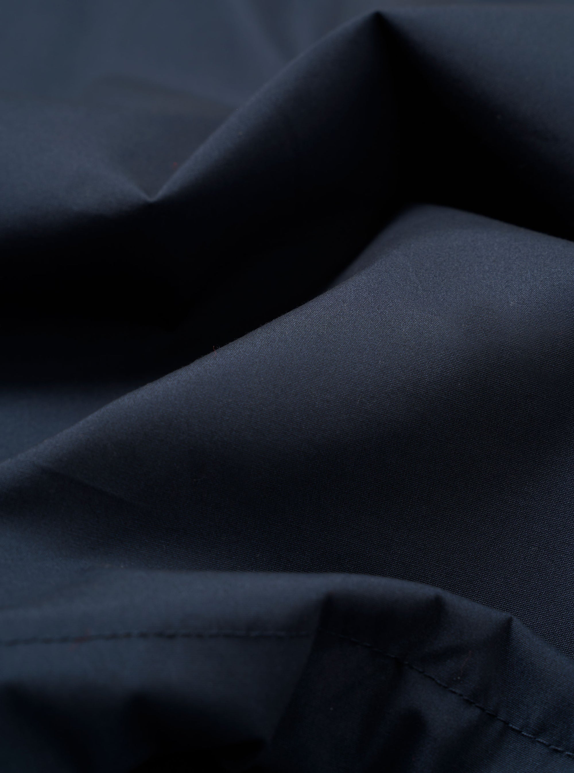 A close-up swatch of the Navy Recycled Polytech Parachute Field Jacket fabric displays a deep navy blue color with a smooth, technical texture. The compact woven material is shown in detail, filling the frame to highlight the utilitarian finish.