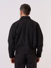 A model is wearing the Black Recycled Polytech Rose Bowl Jacket, shown from a rear three-quarter angle against a plain white background. The jacket features a boxy fit, an oversized collar, and pleats on the back and cuffs. The black fabric has a smooth, utilitarian appearance. No mannequin is present in the image.
