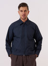 A model wears the Navy Recycled Polytech Rose Bowl Jacket over a light-colored shirt, standing against a plain, neutral studio background. The jacket features a short, boxy fit with a central two-way zip closure and a slightly oversized collar. Prominent details include a large patch pocket on the left chest and two slanted welt pockets at the waist. The smooth, dark navy fabric has a clean, utilitarian appearance. No mannequin is present in the image.