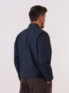 A model wears the Navy Recycled Polytech Rose Bowl Jacket over a light-colored shirt, shown from a side-angle view against a plain white background. The jacket features a classic turn-down collar, a central button-down closure, and a large patch pocket on the front. The navy fabric has a smooth, technical finish.