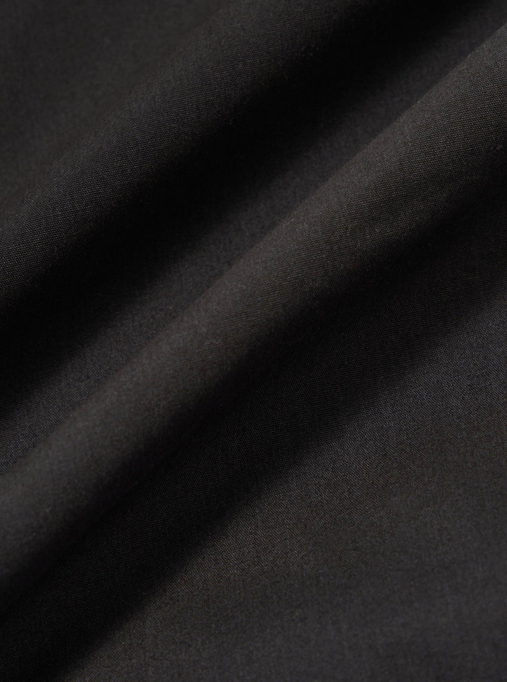 A close-up swatch image of the Black Recycled Polytech Rose Bowl Jacket highlights the smooth, technical texture of the black recycled polytech fabric. The material fills the frame, providing a detailed view of the garment's color and construction.