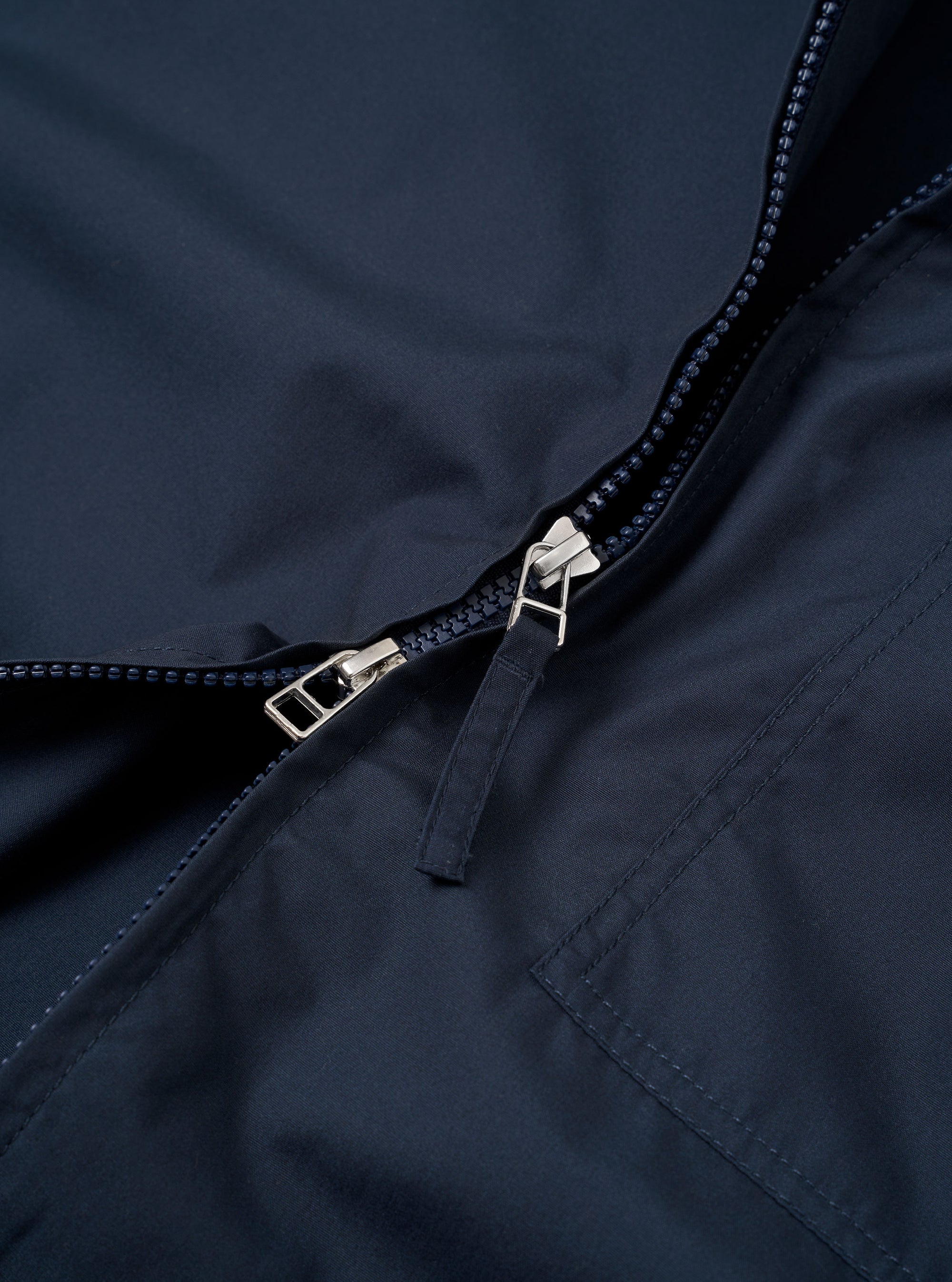 The Navy Recycled Polytech Rose Bowl Jacket is shown from a rear angle as a flat lay against a plain white background. The image highlights the jacket's boxy fit, smooth navy fabric, and adjustable back hem with button detailing.