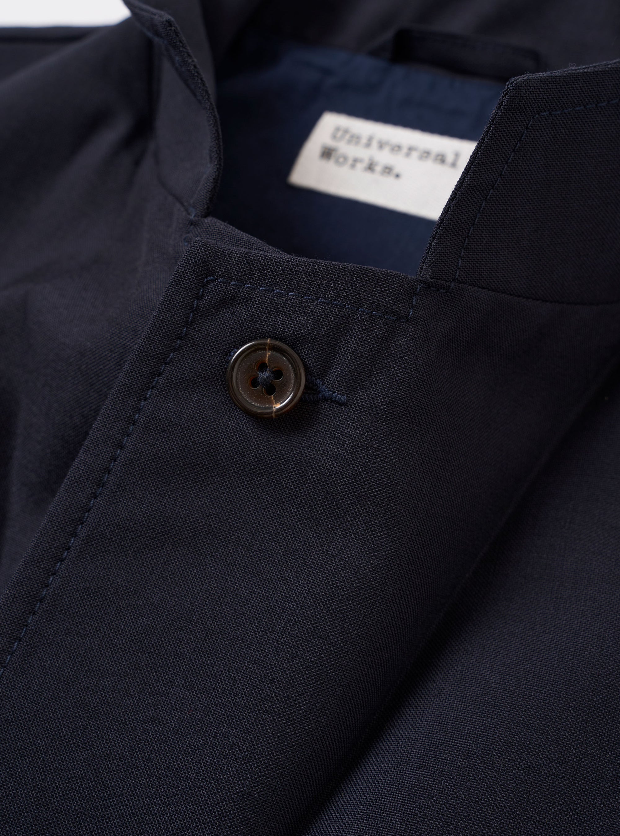 The Navy Tropical Suiting Two Button Jacket is shown from the back as a flat lay against a plain white background. The image highlights the clean, unstructured silhouette of the rear panel, the two-piece sleeves, and the smooth texture of the navy blue tropical suiting fabric.