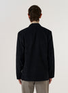 A model wears the Black Organic Fine Cord Two Button Jacket over a light-colored shirt, shown from a rear three-quarter angle against a plain white background. The jacket features a structured back with a central vent and a subtle fine-cord texture. The model is standing with their hands by their sides.