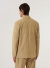 A model wears the Sand Organic Fine Cord Two Button Jacket over a light-colored shirt, standing against a plain white background. The jacket features a relaxed fit with two buttons, a long, wide lapel, two lower patch pockets, and a single chest patch pocket. The fine-ribbed texture of the sand-colored organic cotton corduroy is visible throughout the garment.