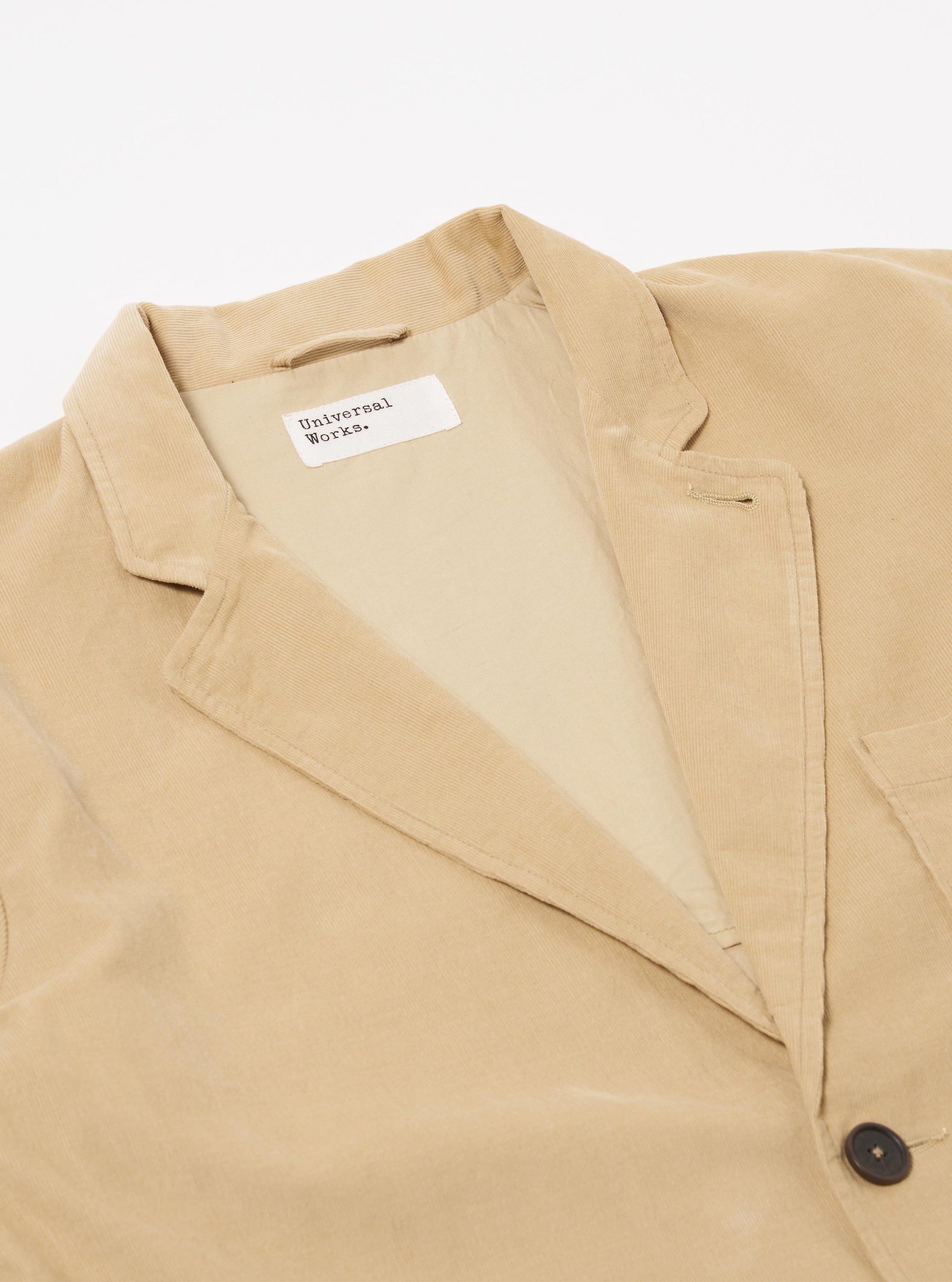 The Sand Organic Fine Cord Two Button Jacket is shown from the rear three-quarter angle as a flat lay against a plain white background. The image highlights the two-piece sleeve construction, the back seams, and the fine-wale texture of the sand-colored organic cotton corduroy.