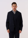 A model wears the Dark Navy Ospina Cotton Two Button Jacket over a light-colored shirt, standing against a plain, neutral background. The jacket features notched lapels, a two-button front closure, and two large patch pockets at the waist. The dark navy fabric has a distinct puckered seersucker texture.