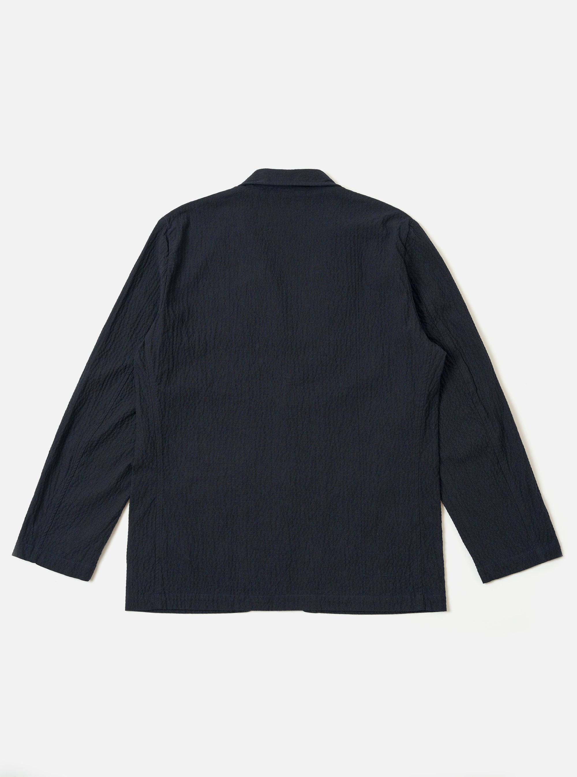 The Dark Navy Ospina Cotton Two Button Jacket is shown from the back as a flat lay against a plain white background. The image highlights the jacket's unstructured design, two-piece sleeves, and the subtle marl effect of the textured navy seersucker fabric.