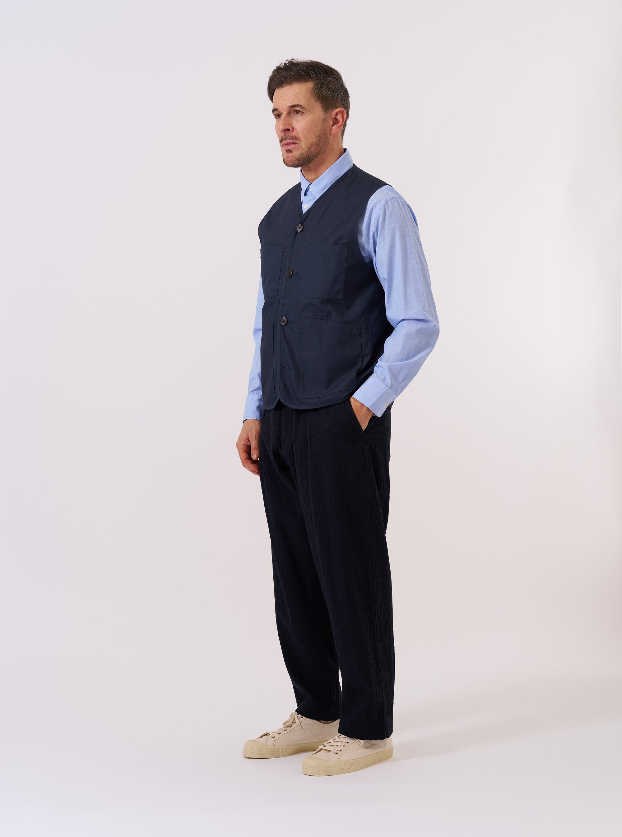 The Navy Recycled Polytech City Waistcoat is displayed as a flat lay against a plain white background. The waistcoat features a V-neckline, a central button-down closure with four buttons, and three front patch pockets including one chest pocket and two larger pockets at the waist. The navy fabric appears smooth with a technical finish.