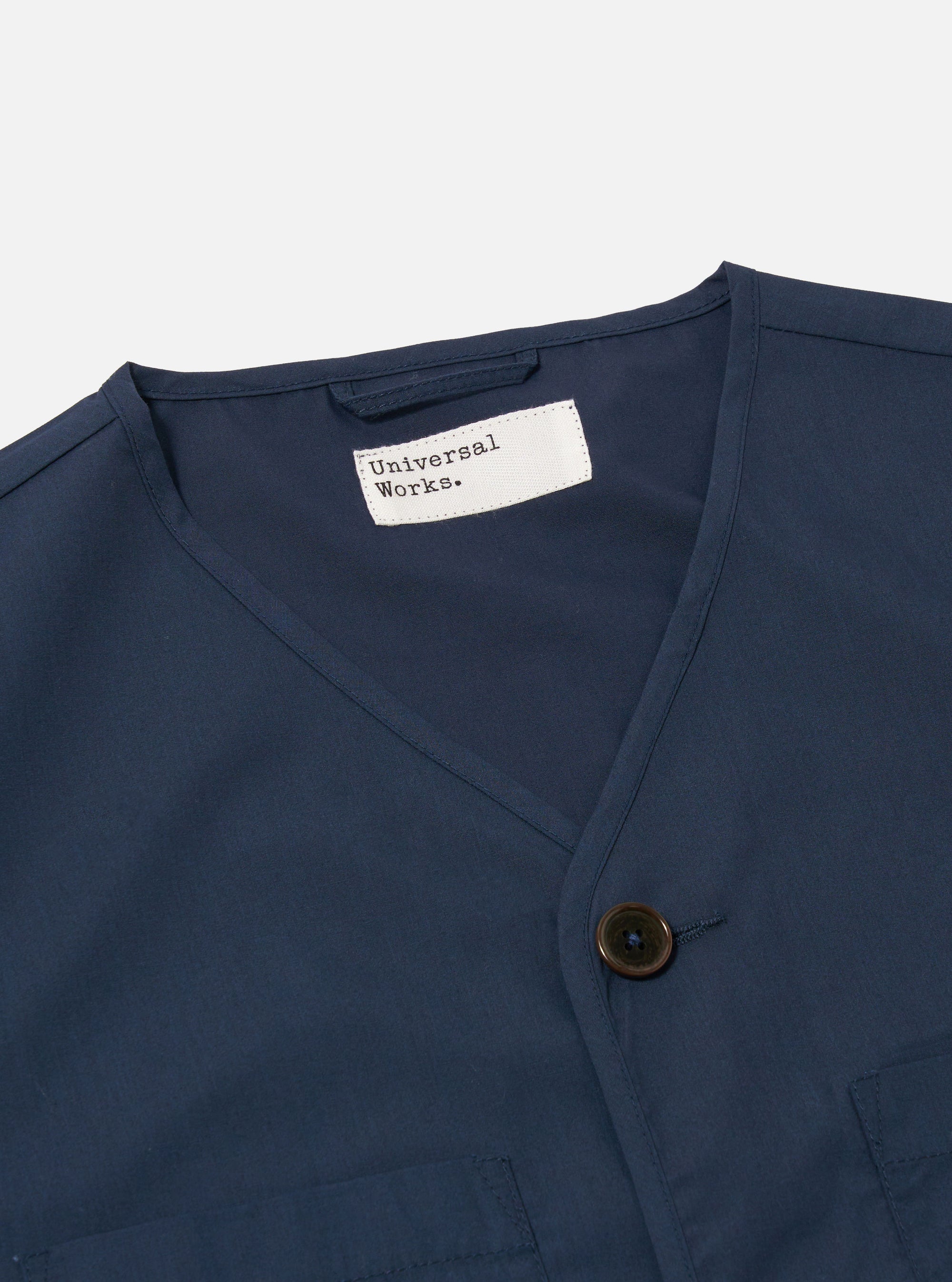 The Navy Recycled Polytech City Waistcoat is shown in a close-up detail shot against a plain white background. The image focuses on the technical texture of the navy blue recycled polytech fabric, highlighting the clean stitching of the pockets and the central button closure.