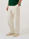 A model wears the Ecru Slub Drill Duke Pant against a plain white background. The model is standing and facing forward, showcasing the loose, wide-leg fit and pleated front of the off-white trousers. The pants are styled with a dark jacket and black shoes.