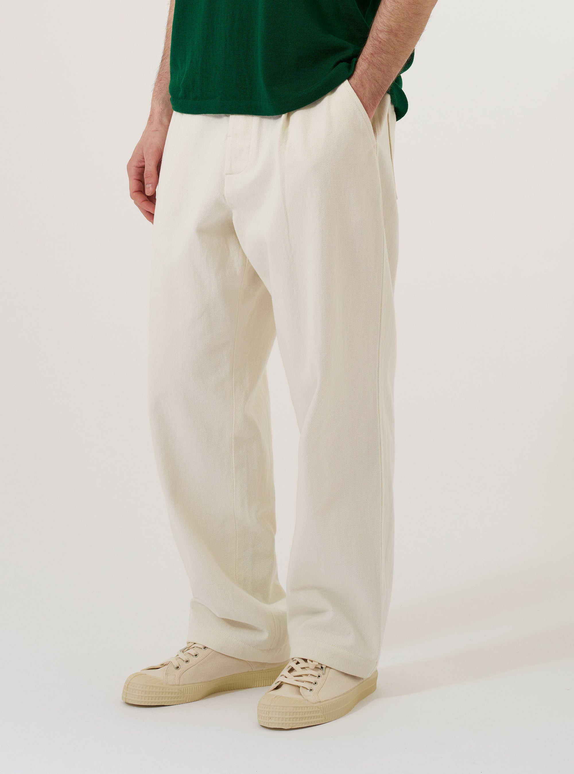 A model wears the Ecru Slub Drill Duke Pant against a plain white background. The model is standing and facing forward, showcasing the loose, wide-leg fit and pleated front of the off-white trousers. The pants are styled with a dark jacket and black shoes.
