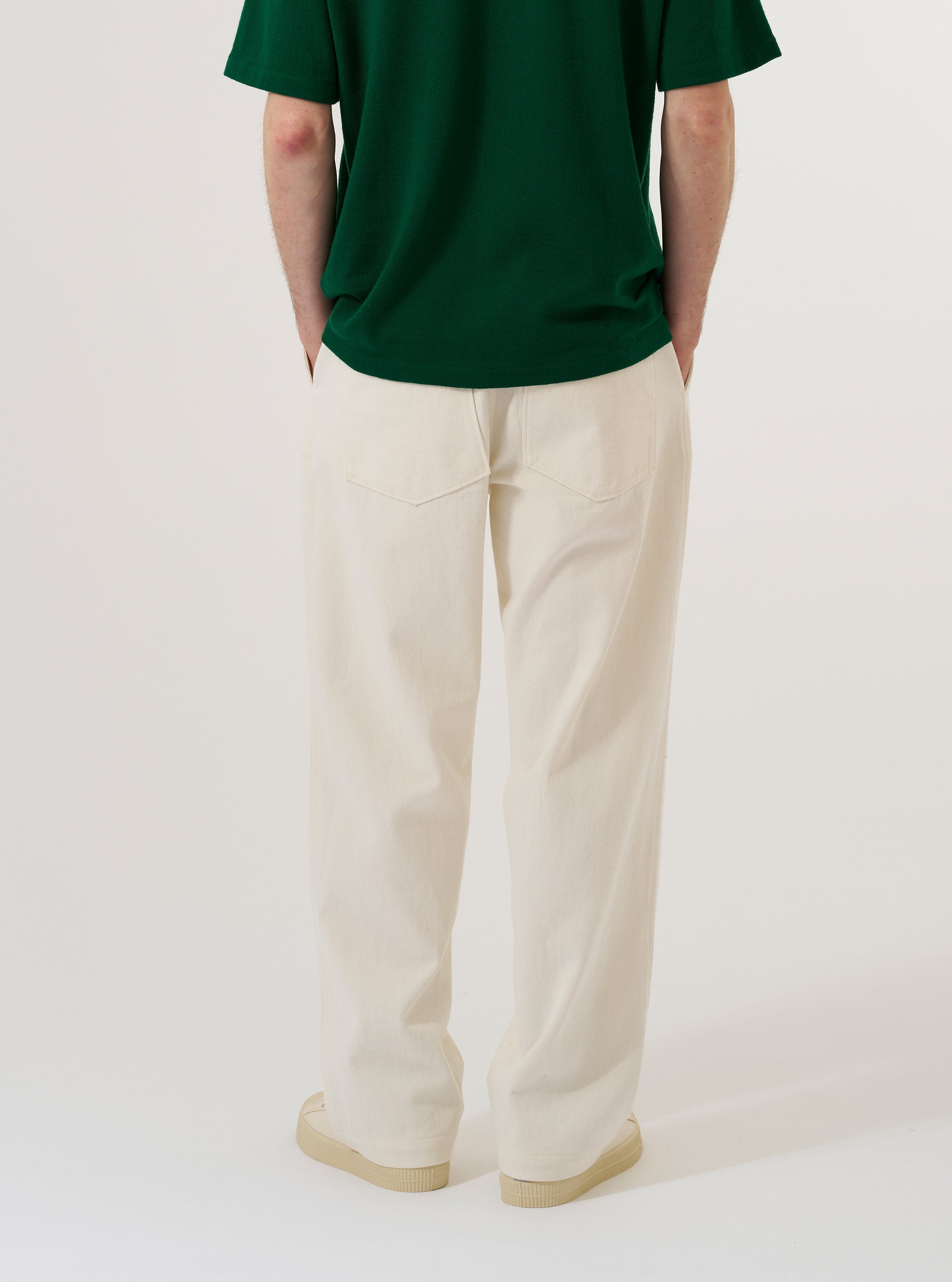 A model wears the Ecru Slub Drill Duke Pant against a plain white background, shown from the waist down in a rear three-quarter view. The image highlights the wide-leg fit, the single rear patch pocket, and the natural, irregular texture of the unbleached ecru cotton fabric.