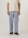 A model wears the Navy Kennedy Stripe Duke Pant against a plain, neutral background. The trousers feature a loose, wide-leg fit and a pleated front, showcasing a distinct vertical navy and white stripe pattern. The model is shown from the waist down, highlighting the drape and silhouette of the cotton garment.
